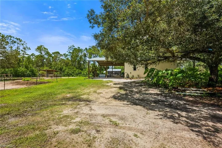 View of yard featuring dirt driveway, a carport, and an outdoor structure