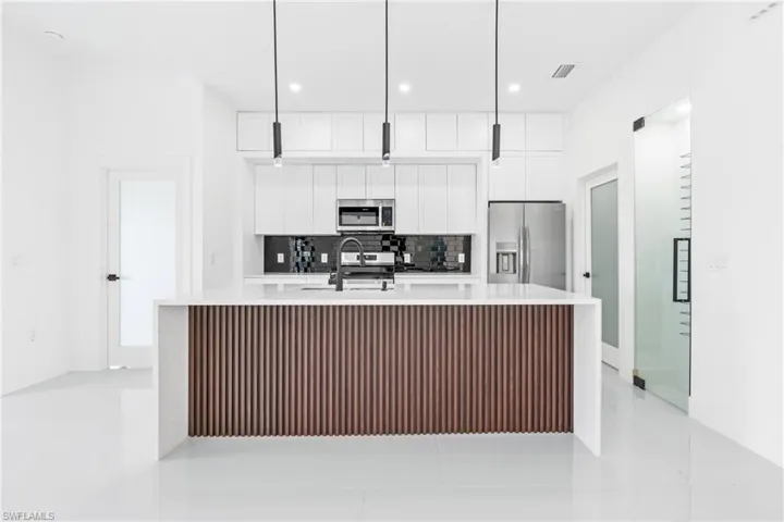Kitchen featuring pendant lighting, appliances with stainless steel finishes, white cabinetry, and an island with sink