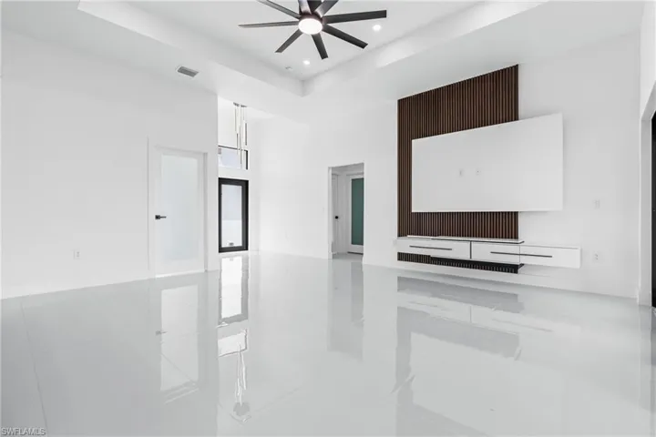 Unfurnished living room with ceiling fan, a tray ceiling, and light tile patterned floors