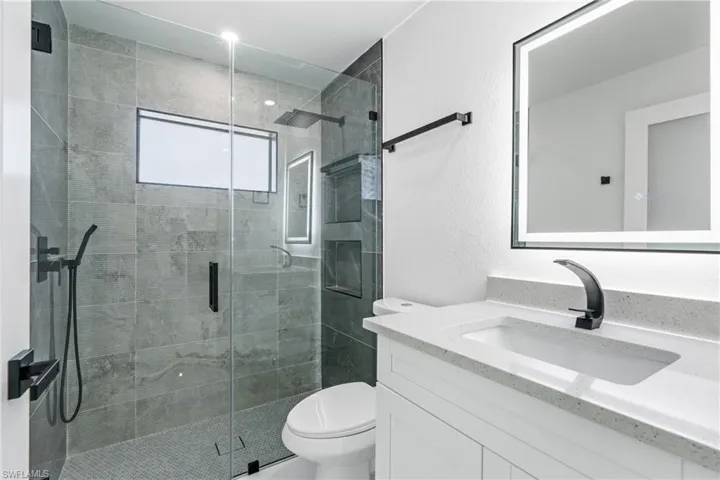 Bathroom with a shower with door, vanity, and toilet
