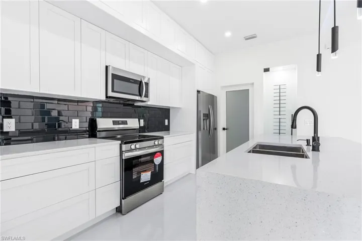 Kitchen featuring stainless steel appliances, backsplash, sink, light stone countertops, and white cabinetry