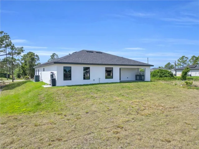 Rear view of house with cooling unit, roof with shingles, stucco siding, and a lawn