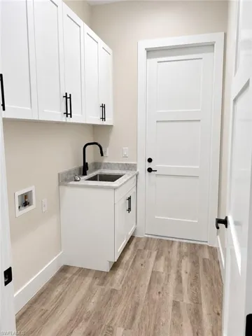 White shaker-style cabinetry with matte black hardware, under-mount sink with black faucet, light wood-finish flooring, and solid core doors