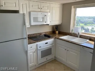 Kitchen with white appliances, dark countertops, white cabinetry, and light tile patterned flooring