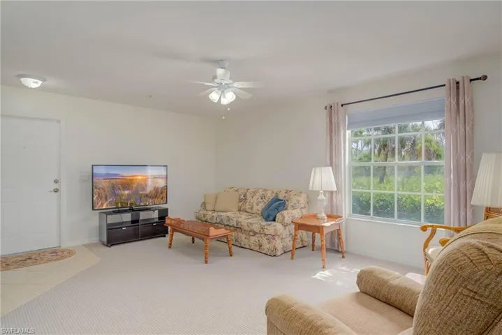 Carpeted living room featuring ceiling fan and baseboards