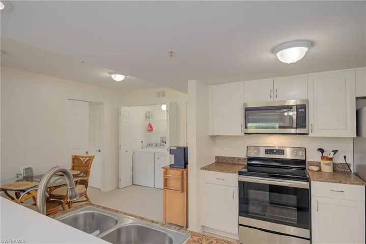 Kitchen with appliances with stainless steel finishes, independent washer and dryer, white cabinets, and dark countertops