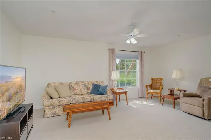 Carpeted living room featuring a ceiling fan and baseboards