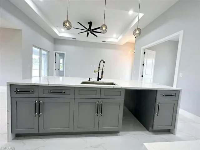 Kitchen with decorative light fixtures, sink, ceiling fan, light tile floors, and a raised ceiling