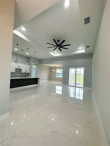 Unfurnished living room featuring sink, ceiling fan, light tile floors, and a raised ceiling