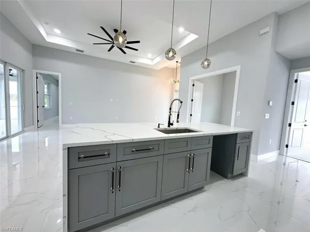 Kitchen featuring ceiling fan, a center island with sink, a raised ceiling, light tile floors, and hanging light fixtures