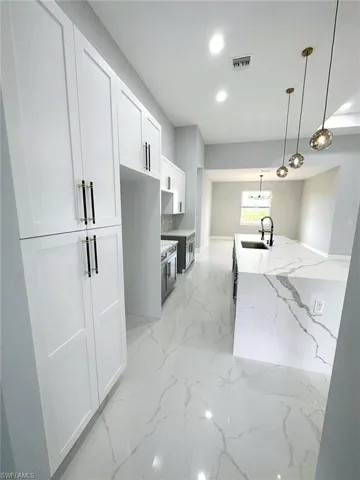 Kitchen featuring light stone countertops, white cabinets, pendant lighting, sink, and light tile flooring