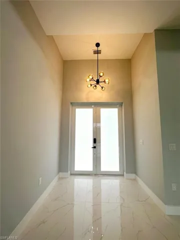 Tiled empty room featuring french doors and a chandelier