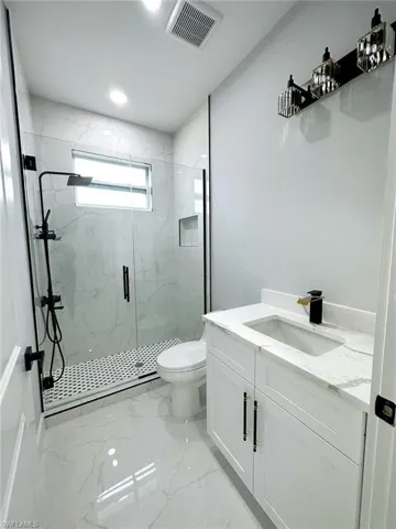 Bathroom with a shower with door, tile flooring, vanity, and toilet