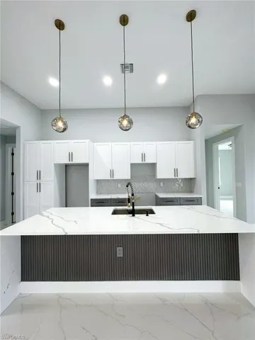 Kitchen featuring hanging light fixtures, light stone countertops, a large island, sink, and tasteful backsplash