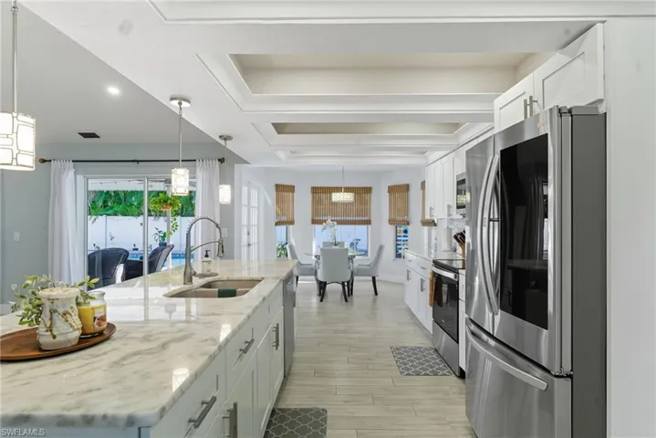 Kitchen featuring stainless steel appliances, white cabinetry, light stone countertops, and decorative light fixtures
