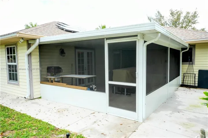 View of side of property featuring solar panels, a sunroom, a shingled roof, and french doors