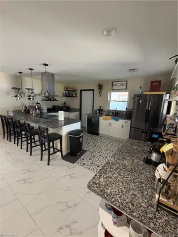 Kitchen with fridge, extractor fan, a kitchen bar, pendant lighting, and white cabinets