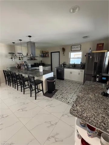 Kitchen featuring fridge, exhaust hood, dishwashing machine, pendant lighting, and white cabinets