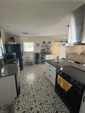 Kitchen featuring sink, stove, white cabinets, dark stone countertops, and exhaust hood