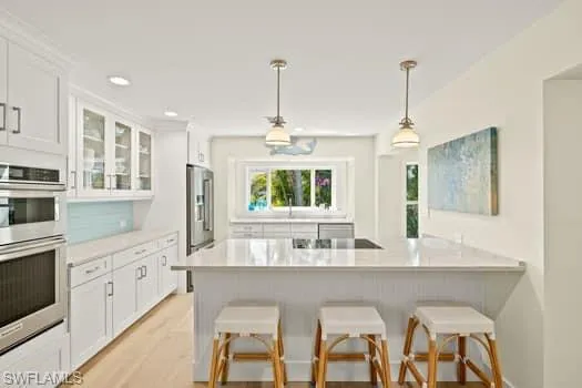 Kitchen featuring glass insert cabinets, appliances with stainless steel finishes, a breakfast bar, and white cabinetry