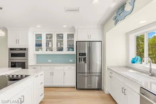Kitchen with glass insert cabinets, light countertops, appliances with stainless steel finishes, white cabinets, and a sink