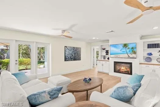 Living area featuring built in shelves, recessed lighting, light wood-style floors, a glass covered fireplace, and a ceiling fan