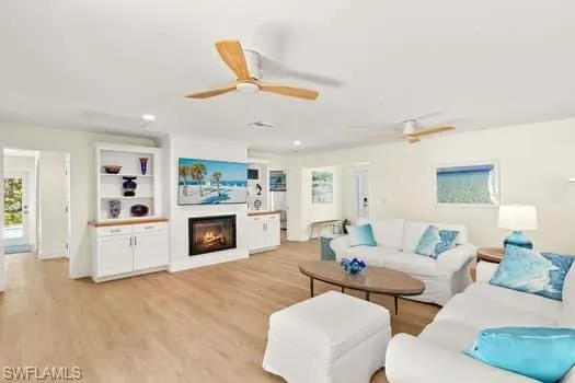 Living area featuring built in shelves, a ceiling fan, recessed lighting, a lit fireplace, and light wood-type flooring