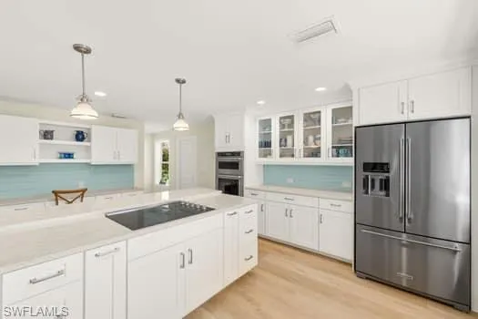 Kitchen featuring stainless steel appliances, white cabinetry, light countertops, and hanging light fixtures
