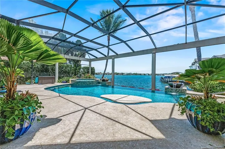 View of infinity pool featuring a pool with connected hot tub, a patio, a lanai, and a water view