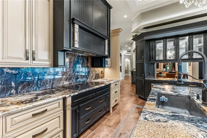 Kitchen featuring tasteful backsplash, cream cabinetry, stone countertops, recessed lighting, and glass insert cabinets