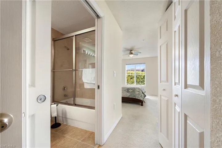Ensuite bathroom featuring combined bath / shower with glass door, light carpet, a textured ceiling, light tile patterned floors, and a ceiling fan