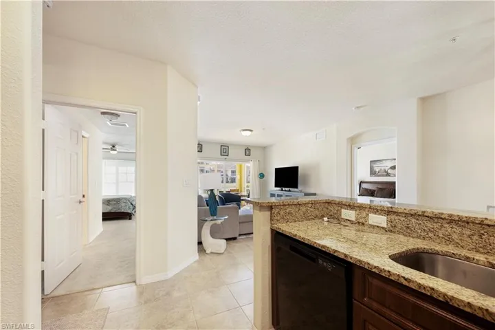 Kitchen with black dishwasher, light stone counters, light colored carpet, dark wood finish cabinets, and open floor plan