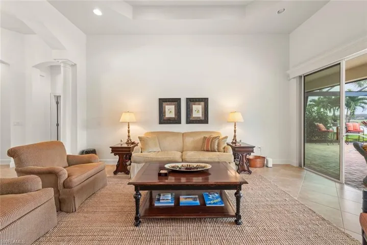 Living area featuring recessed lighting, decorative columns, light tile patterned floors, and a tray ceiling
