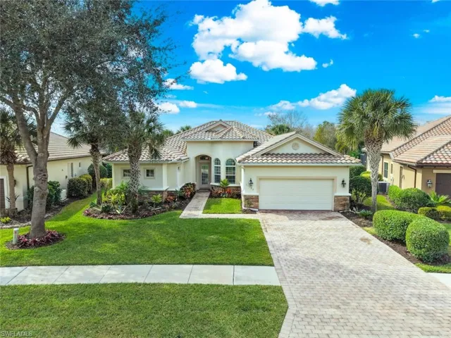 Single family home with a front yard, brick paver driveway, stucco siding and a tiled roof