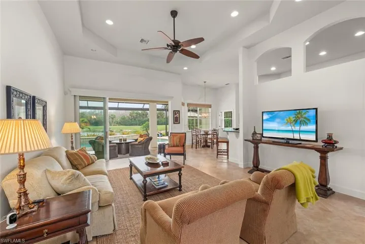 Tiled living area with a tray ceiling, a high ceiling, a ceiling fan, and recessed lighting
