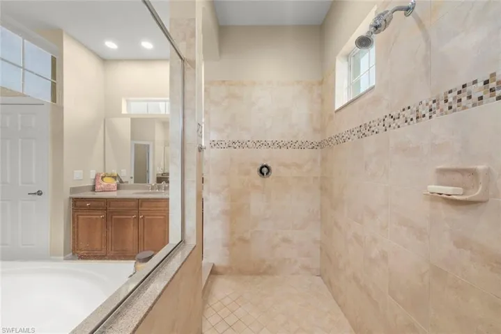 Full bath with walk in shower, vanity, plenty of natural light, a tub, and recessed lighting