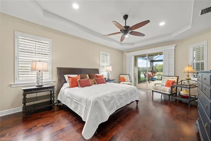 Bedroom with a tray ceiling, access to outside, dark wood-style floors, and ceiling fan