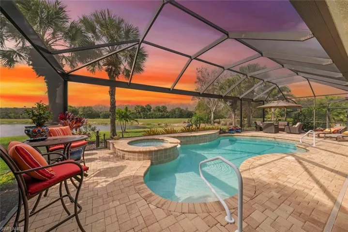 Pool and spa with large screened-in lanai with a picture screen, outdoor seating areas with umbrella and lounge chairs.