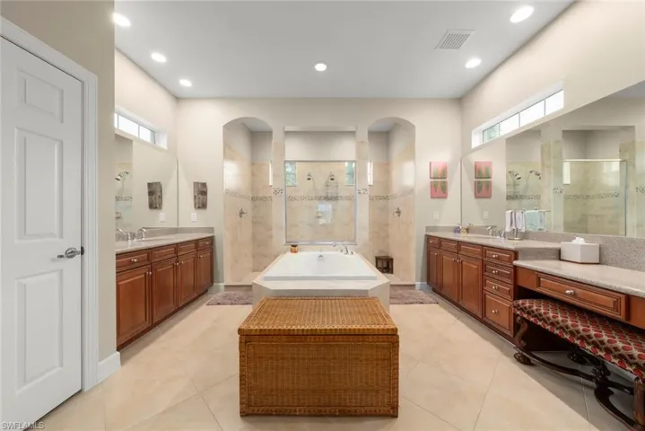 Full bathroom featuring walk in shower, two vanities, a garden tub, light tile patterned floors, and recessed lighting