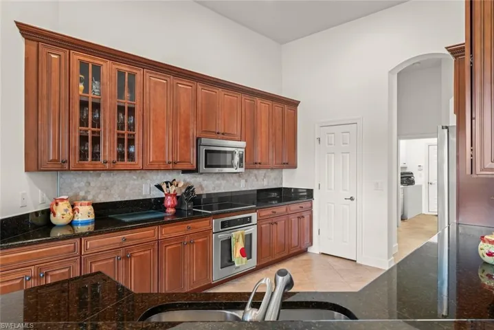 Kitchen featuring stainless steel appliances, pantry, granite counters, backsplash, and a towering ceiling