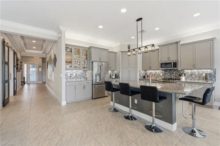 Stunning foyer entry and open kitchen with crown molding, gorgeous glass tile backsplash, glass cabinet door features, built-in pantry, high level cabinets with upper and under cabinet lighting.