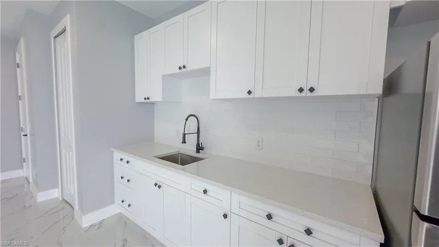 Kitchen with decorative backsplash, light countertops, baseboards, marble finish floor, and a sink