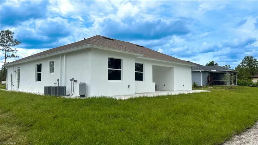 Rear view of house featuring central AC unit, a lawn, and stucco siding