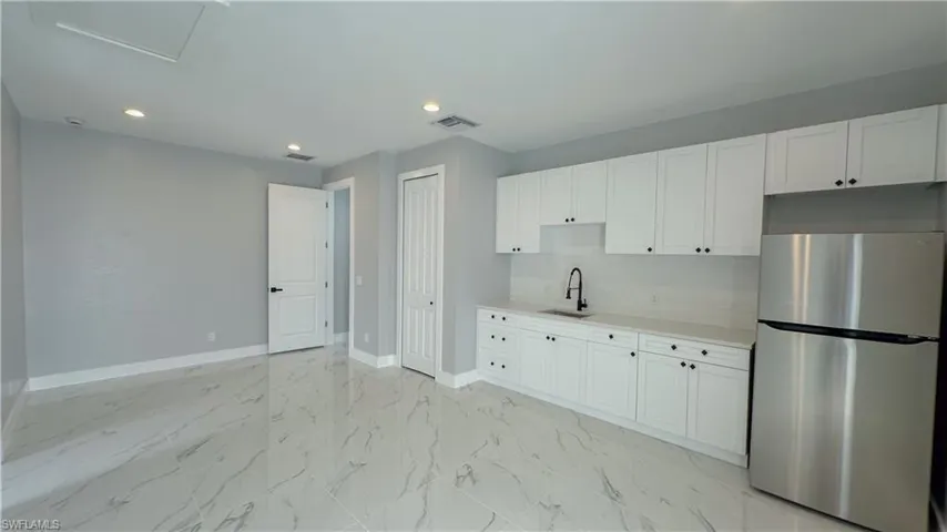 Kitchen with light countertops, marble finish floor, a sink, visible vents, and freestanding refrigerator