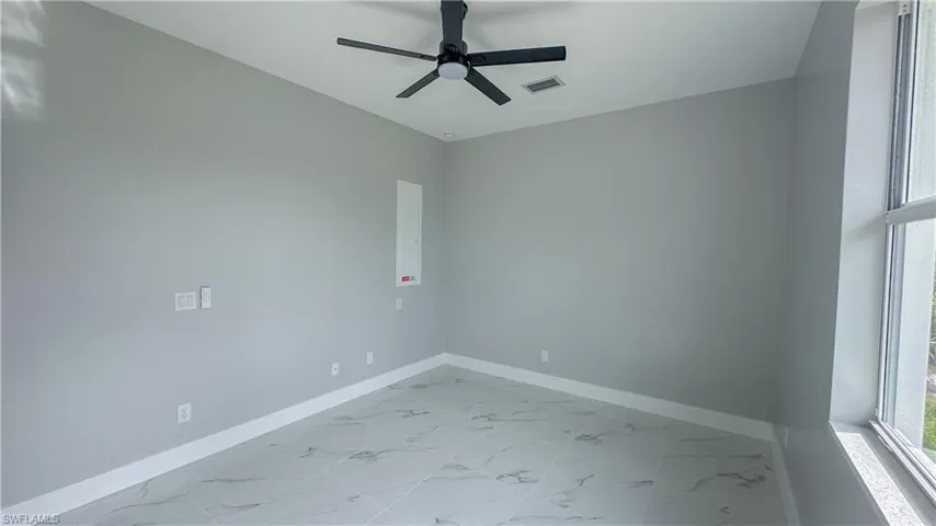 Empty room with marble finish floor, baseboards, visible vents, and ceiling fan