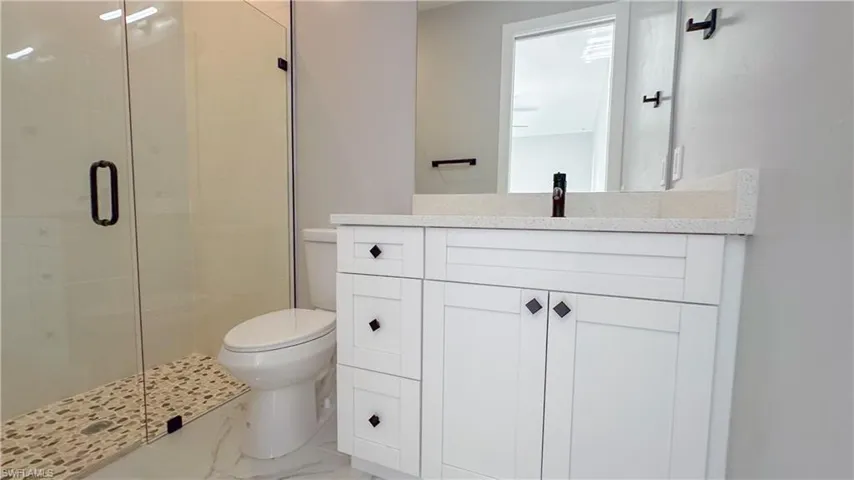 Bathroom with marble finish floor, a stall shower, toilet, and vanity
