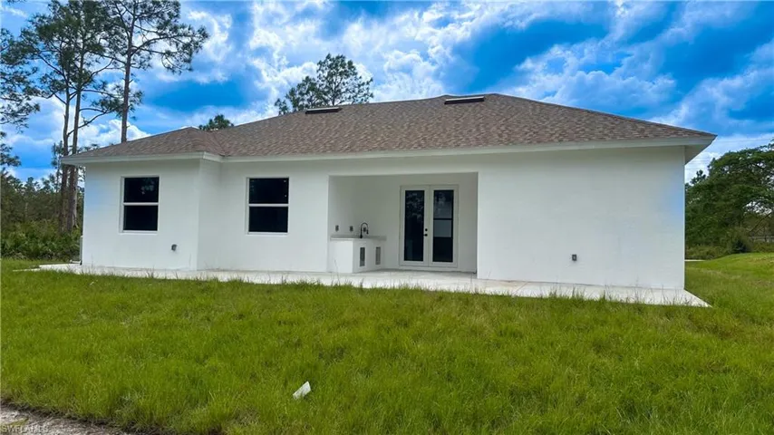 Rear view of property featuring a lawn, a shingled roof, french doors, and stucco siding