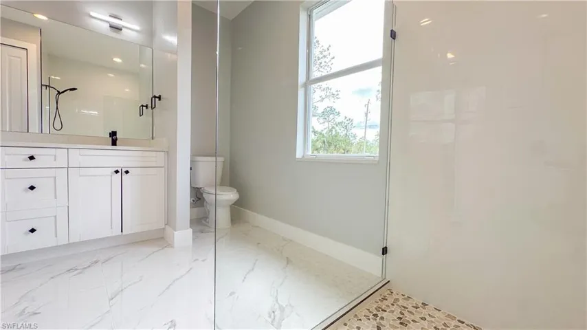 Bathroom featuring vanity, toilet, baseboards, marble finish floor, and a walk in shower