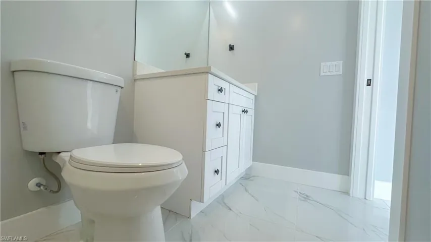 Half bathroom featuring marble finish floor, baseboards, toilet, and vanity