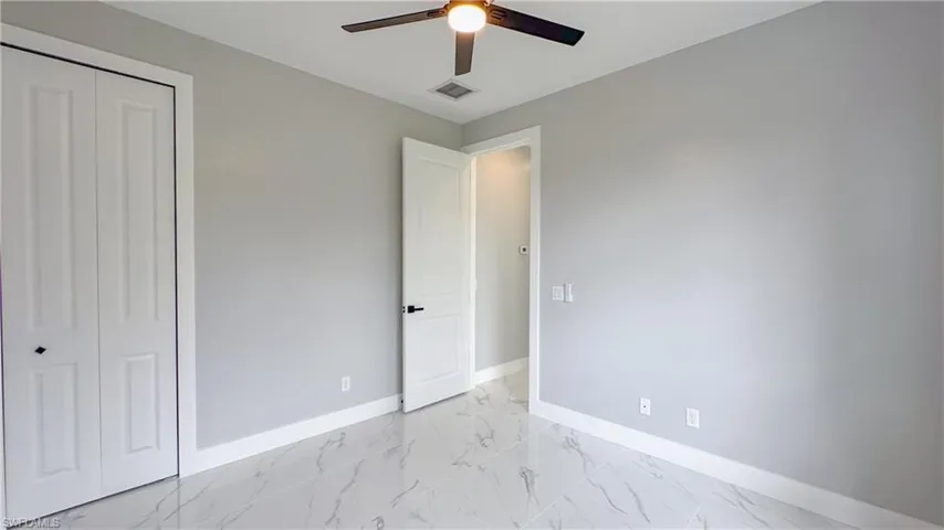 Unfurnished bedroom featuring a closet, a ceiling fan, marble finish floor, baseboards, and visible vents